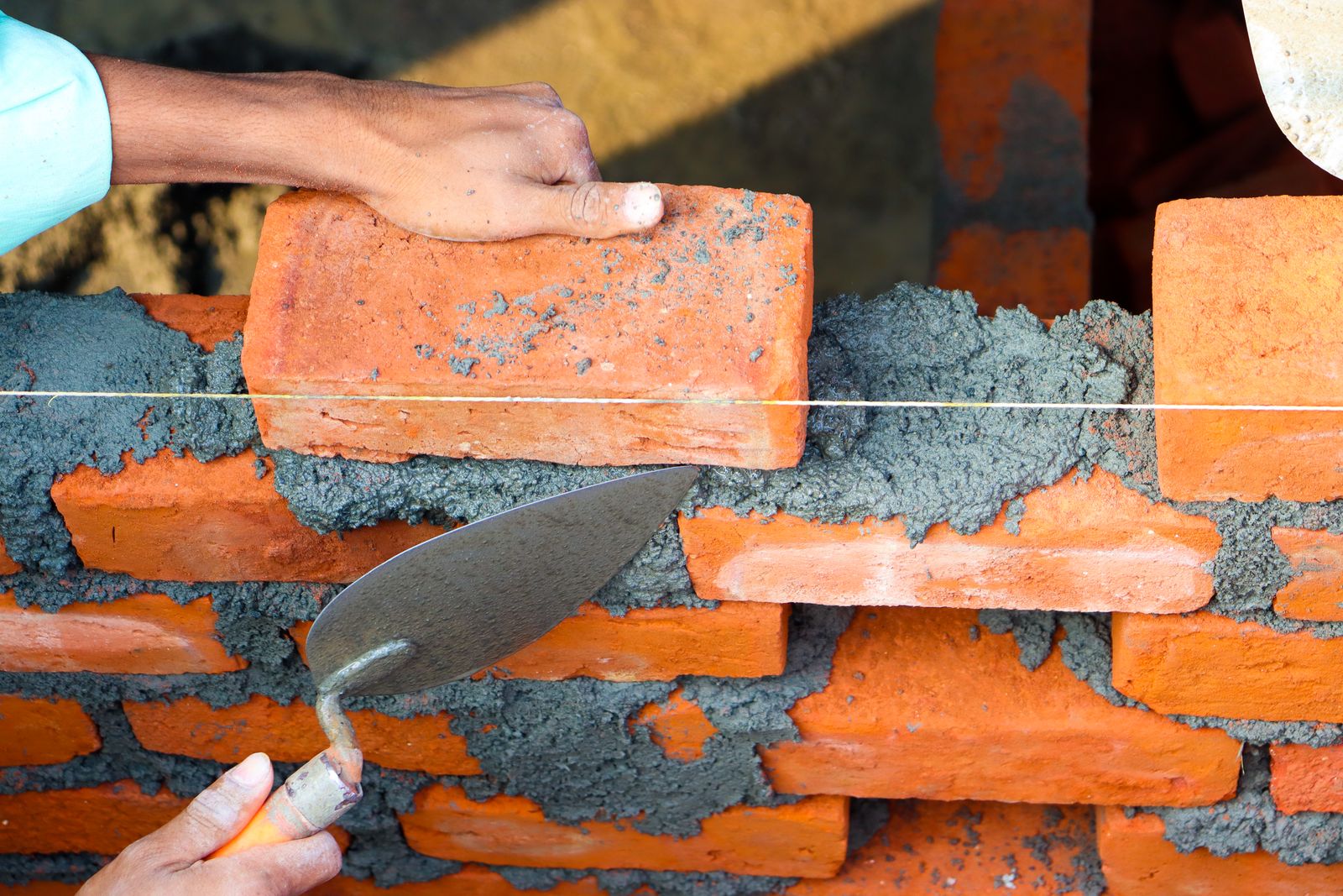 Hands positioning a brick and working mortar with a trowel
